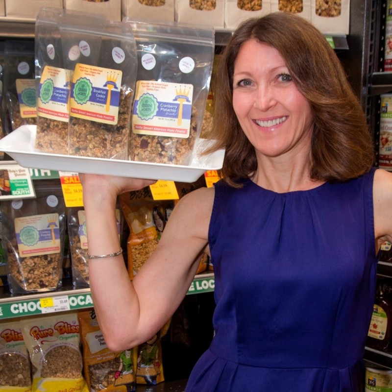 Kelli Swick, owner of Queen of Oats, holds a tray with three bags of her product.